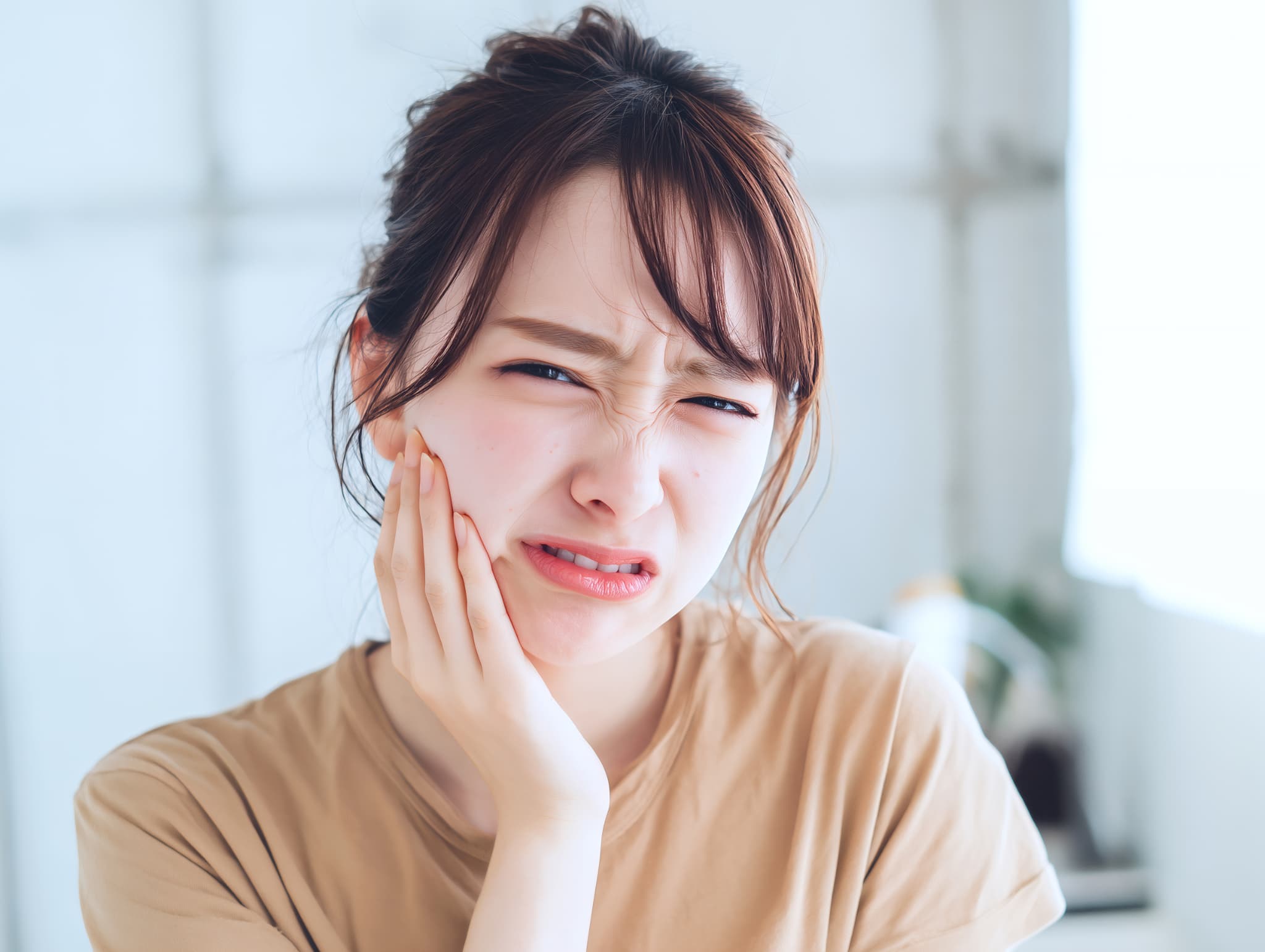 矯正中に歯が痛くなり顔をしかめ頬を押さえる女性