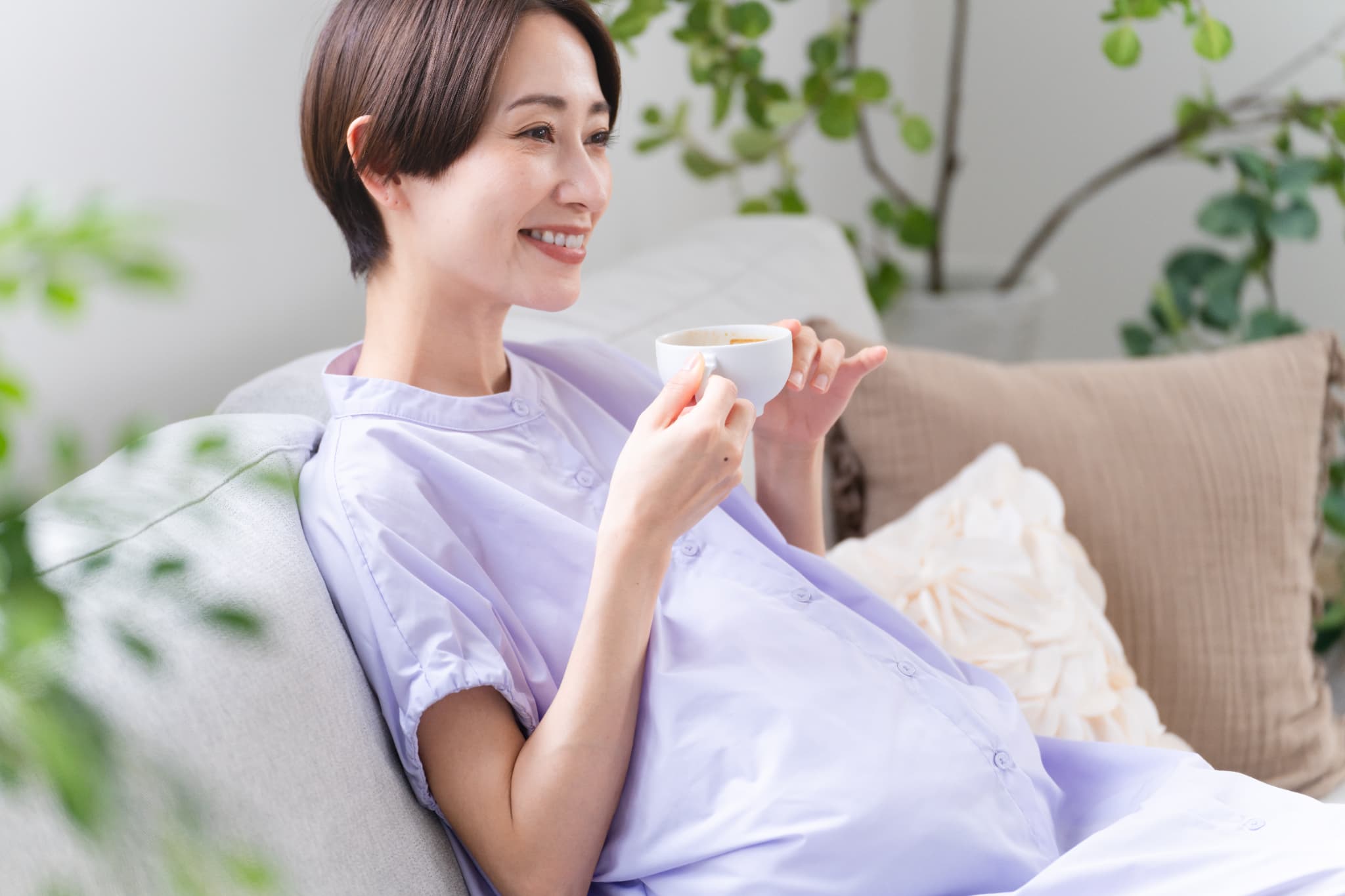 ソファで飲み物を飲んで寛いでいる妊婦